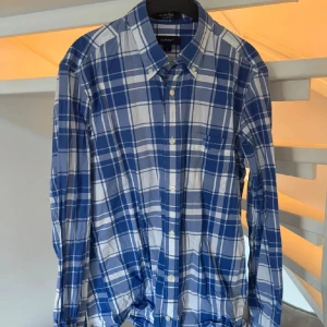 Blårutig skjorta från GANT  - Snygg blårutig skjorta från GANT i regular fit med klassisk krage och knappar framtill. Skjortan har en bröstficka och långa ärmar med manschett. Tillverkad i mjuk bomull, perfekt för dig som gillar stilrena och tidlösa mönster.
