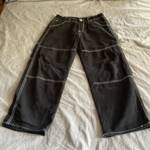 Svarta baggy byxor från H&M - Svarta baggy byxor från H&M med justerbar midja. Snygga kontrastsömmar i vitt ger en cool look. Byxorna har flera fickor både fram och bak, och är tillverkade i ett mjukt bomullsmaterial. Perfekta för dig som gillar streetwear och avslappnad stil. Storlek 158