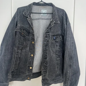 Svart jeansjacka från G Division - Snygg svart jeansjacka från G Division med klassisk krage och coola metallknappar. Jackan har två bröstfickor med lock och logga, samt markerade sömmar som ger en schysst vintagekänsla. Perfekt att slänga över en hoodie för en chill streetstyle.