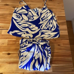 Blå och vit linnetopp med mönster - Snygg linnetopp med tunna axelband i blått och vitt, täckt av ett coolt abstrakt mönster. Toppen har en rak passform och är perfekt för varma dagar. Materialet känns lätt och luftigt, och färgerna är riktigt fräscha och somriga.