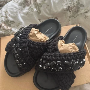 Svarta sandaler Inuikii med pärlor - Säljer ett par svarta sandaler från Inuikii med grovstickade band och coola svarta pärlor och stenar på ovansidan. Sandalerna har platt sula och öppen tå, perfekt för dig som gillar chunky vibes och detaljer. Materialet är stickat textil och syntet.