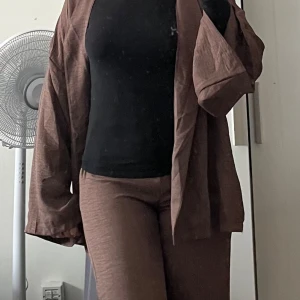 Bruna linnebyxor med rak passform samt brun tröja  - Snygga bruna linnebyxor med rak passform och avslappnad stil. Byxorna har en mjuk och luftig känsla, perfekta för dig som gillar en chill och stilren look. Passar grymt till både t-shirt och skjorta. Färgen är varm brun och materialet är linne. Bruna tröja medföljer då de är ett set !