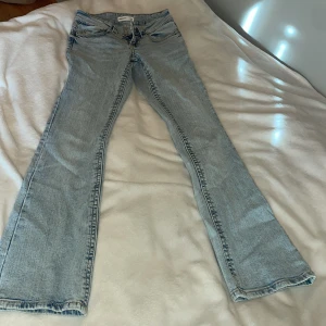 Petite bootcut ljusblå jeans från Gina Tricot - Snygga ljusblå bootcut jeans med låg midja från Gina Tricot i storlek 32. Modellen är petite och har knapp framtill och ljusa sömmar samt fickor bak med knapp på. Jeansen har en väldigt lätt utsvängd passform nedtill. Har en figurnära passform och är stretchiga.