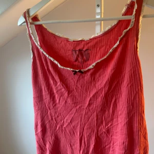 Rosa topp med spetsdetaljer - Supersöt rosa linne från Odd Molly med ribbad struktur och vit spets runt halsringningen. Liten svart rosett framtill ger en gullig touch. Linnet är ärmlös och har en avslappnad passform, perfekt för varma dagar.