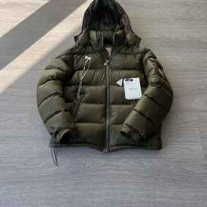 Moncler Maya olive  - Säljer denna olivgröna moncler maya då den inte passar längre. Den går att skanna och lappar och sådant följer med som ni ser på bilden. Det är storlek 1 som motsvarar S. Den har två jättesmå hål på högra armen och därmed säljer jag billigt. Fråga vid minsta funderingar😊