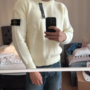 Vit stickad tröja från Stone Island - Säljer en clean vit stickad tröja från Stone Island med klassisk patch på vänster ärm. Tröjan har rund hals, ribbade muddar och en relaxed passform. Perfekt för dig som gillar stilrena plagg med street-vibe och vill ha något som funkar till jeans.