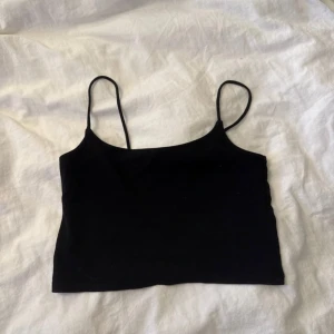 Svart croppad linnetopp med smala band - Svart croppad linnetopp från Weekday med smala axelband och enkel, stilren design. Perfekt för dig som gillar minimalistisk stil och vill ha en topp som är lätt att matcha med allt. Mjuk bomullskänsla och figurnära passform.