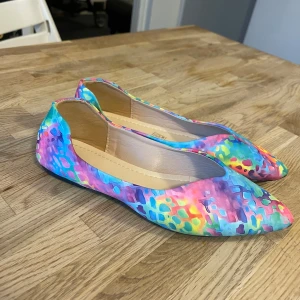 Färgglada ballerinaskor med spetsig tå - Säljer ett par ballerinaskor med spetsig tå i ett riktigt färgsprakande mönster. Skorna har en mix av blå, rosa, lila, gul och gröna toner med ett abstrakt mönster som ger dem en unik vibe. Yttermaterialet är syntet och sulan är platt, perfekt för dig som gillar att sticka ut.Eu storlek 39