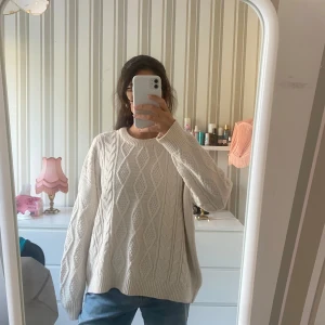 Oversized kabelstickad vit tröja - Säljer en oversized kabelstickad tröja i mjuk vit färg med grovt mönster av flätor och diamantformer. Tröjan har rund hals, långa ärmar och breda muddar. 