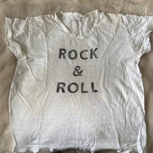 Vit t-shirt från Zadig & Voltaire - Vit t-shirt från Zadig & Voltaire med trycket 'ROCK & ROLL' i svart på framsidan. Klassisk rund hals och korta ärmar. T-shirten är gjord i mjuk bomull och har en avslappnad passform som är perfekt för en cool och casual stil.