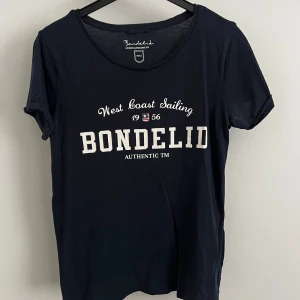 Mörkblå t-shirt från Bondelid - Mörkblå t-shirt från Bondelid med vit text på bröstet. Klassisk rund halsringning och korta ärmar. Perfekt för en avslappnad stil.