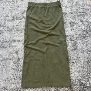 Olivgrön långkjol  - Säljer en olivgrön långkjol från Pieces i ribbad bomullskvalitet. Kjolen har en rak passform, resår i midjan och en slits på sidan. Perfekt att styla med en enkel topp eller hoodie. Nästan som ny, tror jag använt den en gång bara. 