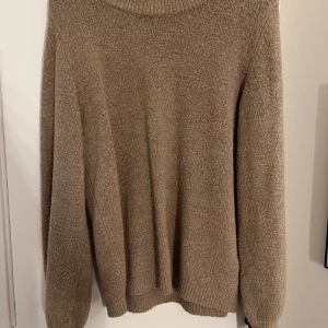 Beige stickad tröja med rund hals - Mysig beige stickad tröja med rund hals och långa ärmar. Tröjan har en enkel och klassisk design med ribbade muddar vid ärmslut och nederkant. Perfekt för lager-på-lager och passar till många olika outfits.