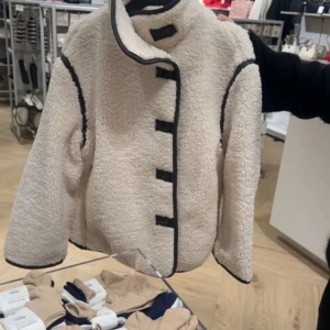 Vit teddyjacka med svarta detaljer - Supermysig vit teddyjacka med mörkbruna kantdetaljer och knäppning fram. 