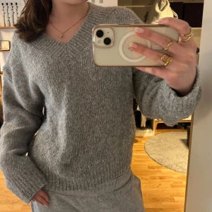 Grå stickad tröja från H&M Divided - Mysig grå stickad tröja från H&M Divided med v-ringning och långa ärmar. Tröjan har en avslappnad passform och ribbade muddar vid ärmslut och nederkant. Perfekt att ha över på svala sommarkvällar. 🤍