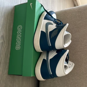 Nike Air Jordan 1 Mid blå och vita - Säljer ett par Nike Air Jordan 1 Mid i blått och vitt. Skorna har klassisk hög siluett, snörning och den ikoniska vingen på sidan. Perfekta för dig som gillar streetwear och sneakers med retrostil.