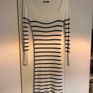 Vit ribbad klänning med svarta ränder - Säljer en vit ribbad klänning med svarta horisontella ränder. Klänningen har lång ärm, rundad halsringning och är figurnära i modellen.