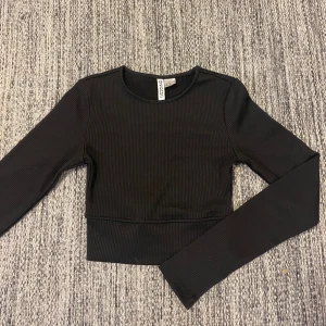 Svart croppad träningstopp  - Säljer en ribbad croppad träningstopp från H&M. Den är långärmad, har rund halsringning och ett stretchigt material. Använd 1 gång 💗