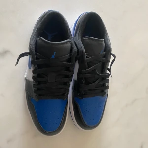 Nike Air Jordans Low blå och svarta sneakers - Säljer ett par Nike Air Jordans Low med svart, blå och vit färg. Skorna har klassisk snörning, rund tå och platt sula. Andvända 1 gång på test. (BOX INGÅR) 