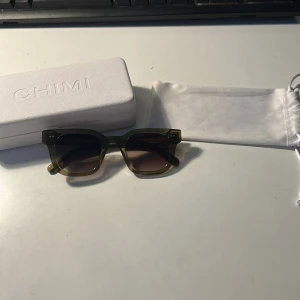 Gröna solglasögon från CHIMI - Snygga solglasögon från CHIMI i modell 04 i transparent grön färg med fyrkantig form. Glasögonen har mörka linser och en stilren design. Perfekta för soliga dagar och levereras med originalfodral och påse. Inga defekter på dem