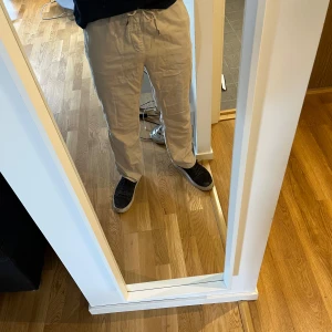 Baggy chinos från East west - Vita/beige byxor som är raka/baggy till formen, men har fortfarande ett lite mer formell/mer chinos aktigt material - jämfört med vanliga linnebyxor. Byxorna är använda ett fåtal gånger och är i nyskick. Det är inte dragkedja eller knappar på dem, de sitter bra som de är och dras åt med snören (likt linnebyxor).