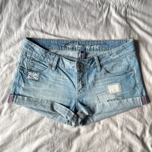 Low-waist jeansshorts från edc esprit - Ljusblå jeansshorts från edc esprit med patchade detaljer och uppvikta benslut. Klassisk femficksmodell med knapp och dragkedja. Snygga broderade detaljer. Mått tvärsöver midjan 42 cm 💕