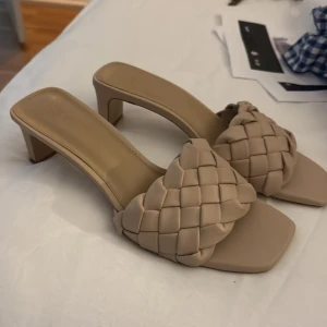 Beige flätade sandaler med klack - Säljer ett par trendiga beige sandaler med fyrkantig tå och flätad rem över foten. Skorna har en medelhög klack och öppen tå, perfekta för vår och sommar. Snygg och stilren design som passar till många outfits.