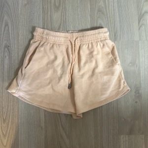 Aprikos färgade shorts med dragsko från H&M - Mjuka aprikosfärgade shorts från H&M med elastisk midja och dragsko. Shortsen har fickor på sidorna och är tillverkade i ett bekvämt material som passar perfekt för varma dagar.