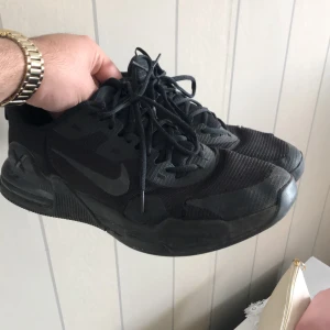 Svarta Nike sneakers - Säljer ett par helsvarta Nike sneakers med snörning och rund tå. Skorna har en sportig design med mesh och syntetmaterial, perfekt för dig som gillar en clean och stilren look.