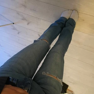 Blå slitna jeans med hål på knäna - Säljer ett par blå jeans med hål på knät samt låret. Jeansen har klassisk femficksdesign och är raka i modellen. Perfekta för en avslappnad och trendig look.