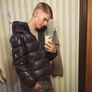 Mörkblå dunjacka från Moncler - Säljer en mörkblå Moncler dunjacka med huva och klassisk logotyp på ärmen. Jackan har quiltad design, dragkedja framtill och två sidofickor med dragkedja. Insidan har ett serietidningsmönster och autenticitetsmärke. Jackan håller lätt värmen under kyligare dagar samt ger en lyxig look. Dock  så har tidningen lossnat! Jackan är oginal!  7-10 kom med pris förslag nfc fungerar!  Öppen för byten! Finns i Hässleholm/ Kristianstad. Dm för frågor och funderingar, för fler bilder kom dm!
