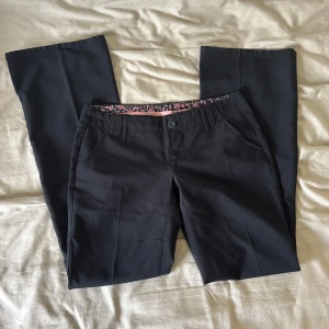 Svarta kostymbyxor från Esprit - Snygga svarta kostymbyxor från Esprit med klassisk passform och knappstängning. Insidan av linningen har ett blommigt tyg i rosa och svart. Midjemått 40cm rakt över. Innerbenslängd 83cm.