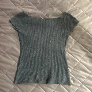 Grå ribbad topp från H&M - Säljer en grå ribbad topp från H&M med korta ärmar och rund halsringning. Toppen är stretchig och har en tight passform, perfekt att styla till olika outfits. Ärmarna går att dra ned så att de sitter på överarmen istället för axlarna
