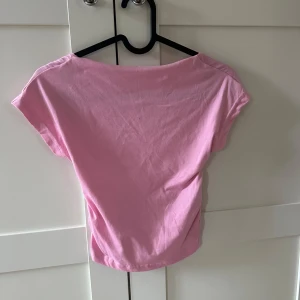 Ljusrosa topp med öppen rygg - Säljer en ljusrosa topp med öppen rygg som är tillverkad i mjukt bomullsmaterial. Perfekt att styla över linne eller klänning för en trendig look.