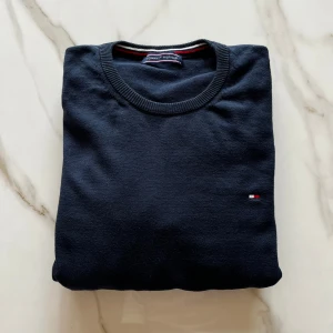 Mörkblå tröja från Tommy Hilfiger - Säljer en klassisk mörkblå tröja från Tommy Hilfiger med rund halsringning och diskret broderad logga på bröstet. Tröjan har långa ärmar och är tillverkad i mjuk bomull, perfekt för en stilren look.