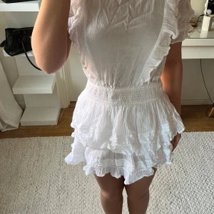 Vit volangklänning med resår i midjan - Superfin vit klänning med volangdetaljer och korta ärmar. Klänningen har resår i midjan och dubbla volanger på kjolen för extra volym. Perfekt för sommarens alla tillfällen! Den är från Gina Young, jag bör vanligtvis xs/s