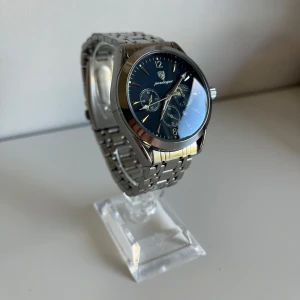 Silverfärgad klocka från Poedagar - Stilren klocka från Poedagar med blå urtavla och silverfärgat armband i metall. Klockan har tre mindre urtavlor och tydliga siffror. Perfekt accessoar för dig som gillar klassisk design.