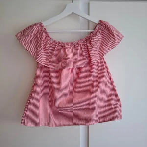 Röd- och vitrandig offshoulder topp - Säljer en söt offshoulder topp med röda och vita ränder. Toppen har en bred volang runt axlarna och är perfekt för varma dagar. Luftig och lätt att matcha med jeans eller kjol.