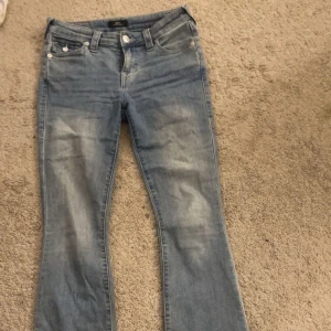 True Religion BECCA Mid Rise Bootcut Jeans - Säljer ett par ljusblå jeans från True Religion, modell BECCA med midwaist och bootcut. Då jag inte använder dom och är intresserad av att köpa annan färg! Jeansen har klassiska fickor med lock och knappar bak. 