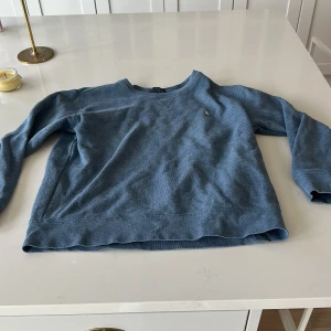 Blå tröja från Polo Ralph Lauren - Säljer en blå långärmad tröja från Polo Ralph Lauren. Tröjan har en klassisk passform och är tillverkad i mjuk bomull. Liten broderad logga på bröstet. Perfekt för en avslappnad och stilren look.