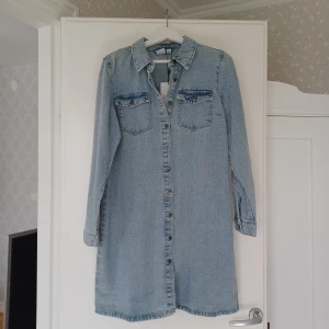 Ljusblå jeansklänning från Vero Moda - Säljer en ljusblå jeansklänning från Vero Moda med klassisk skjortkrage och knäppning framtill. HELT NY o jag köpte den för 549 kr. Jag har vanligtvis storlek 38 men denna är perfekt. 