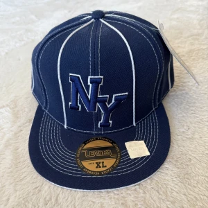 Blå keps med vita ränder  - Säljer en blå keps från Leader med vita vertikala ränder och broderad NY-logga framtill. Kepsen har platt skärm och klassisk basebollstil. Märke och storleksetikett sitter kvar. Skulle nog säga storleken på den är 60-62, säljer den eftersom den var stor