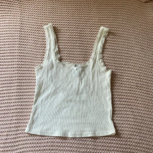Vit ribbad linnetopp med spets från H&M Divided - Supersöt croppad vit och ribbad linnetopp från H&M Divided med spetskant runt ringningen och axelbanden. Liten rosett framtill som extra detalj. Perfekt att styla med jeans eller kjol för en fräsch look💞