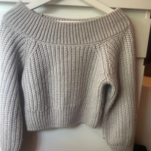 Ljusgrå stickad offshoulder-tröja - Supermysig ljusgrå stickad tröja med bred ribbad kant och offshoulder-modell. Perfekt för lager-på-lager och ger en chill vibe. Tjockt garn och långärmad design gör den extra varm och skön under kyliga dagar.
