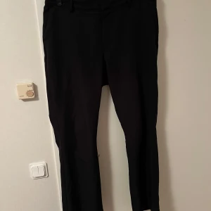 Svarta kostymbyxor från Bik Bok - Snygga svarta kostymbyxor från Bik Bok i klassisk rak modell. Byxorna har hällor för bälte och sidfickor, perfekta för en clean och stilren look. Passar dig som gillar enkel och tidlös stil.