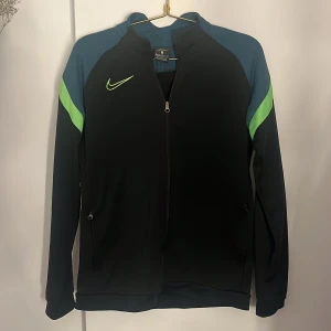 Nike träningsjacka - Säljer denna Nike träningsjacka då den inte kommer till användning lägre. Den är i storlek xl i barnstorlek så den är inte som en xl i vuxenstrolek. Den är tunnt fodrad så det går bra att ha på sig den ute i lite kyligare väder