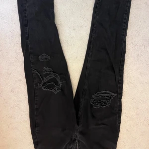 Svarta ripped jeans från Zara - Passar xs-s.                                                            Svarta jeans från Zara med snygga slitningar och hål på båda benen. Modellen är slim och har en klassisk femficksdesign. Perfekta för en edgy och trendig look. Tillverkade i mjuk bomullsdenim med lite stretch för extra komfort.