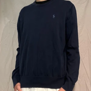 Finstickad tröja från Polo Ralph Lauren - Snygg mörkblå tröja från Polo Ralph Lauren i 100% pima bomull. Klassisk rund halsringning och diskret broderad logga på bröstet. Perfekt basic med lång ärm och relaxed fit, passar till allt och är superbekväm.