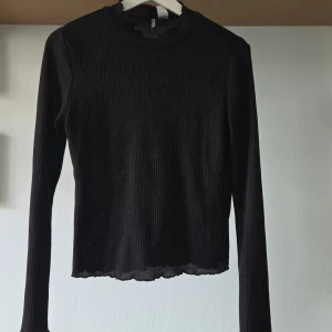 Svart ribbad långärmad topp H&M Divided - Svart långärmad topp från H&M Divided i ribbad, stretchig polyester. Tight passform med rund hals och vågig kant nertill. Något genomskinlig beroende på vad man har under. 
