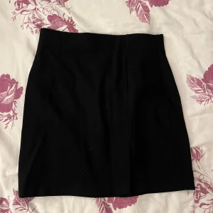 Svart kortkjol från Stradivarius  - Enkel och stilren svart kortkjol från Stradivarius i storlek XS. Kjolen har en rak passform och har en liten slits. Gjord i ett mjukt och stretchigt material som sitter snyggt i midjan.